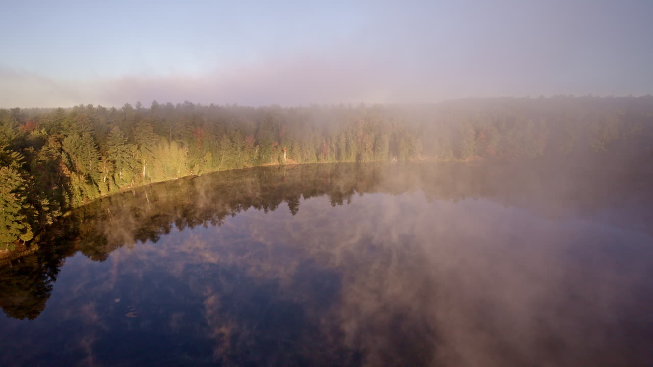 Drone perspective of dawn mist slowly rising above the water