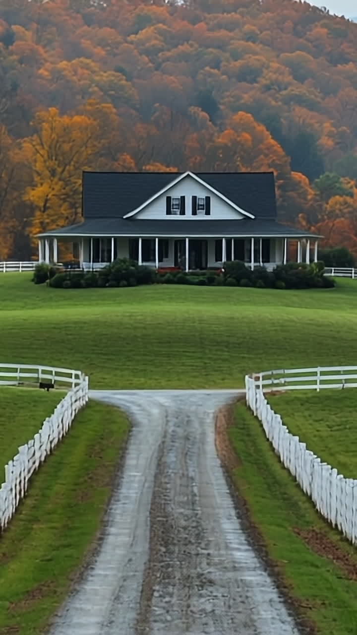 Autumn trees by country house. A serene house sits on a hill, framed by vibrant autumn foliage and a winding gravel path, under a blue sky.