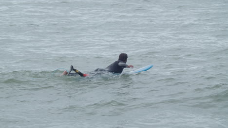 Hombre-Deportivo-En-Traje-De-Neopreno-Con-Pierna-Artificial-Acostado-En-La-Tabla-De-Surf-Y-Nadando-En-El-Océano-5