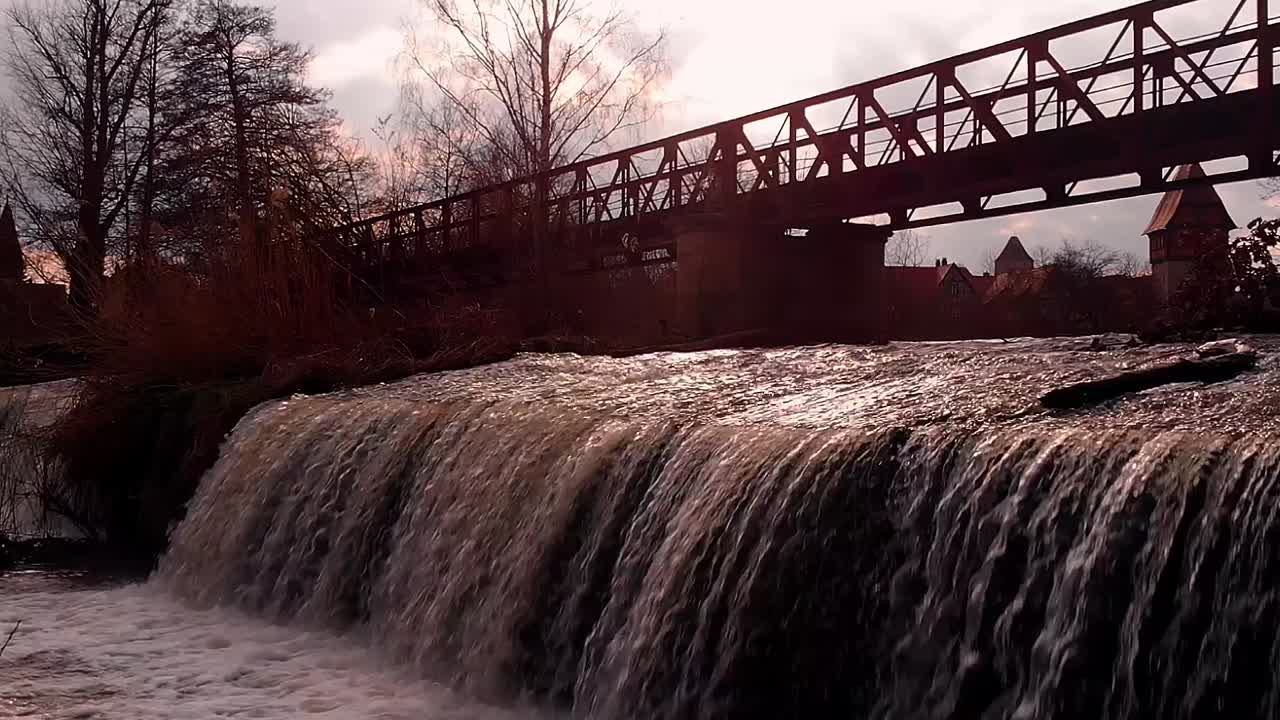 aerial approaches the waterfall and the bridge at the sunset