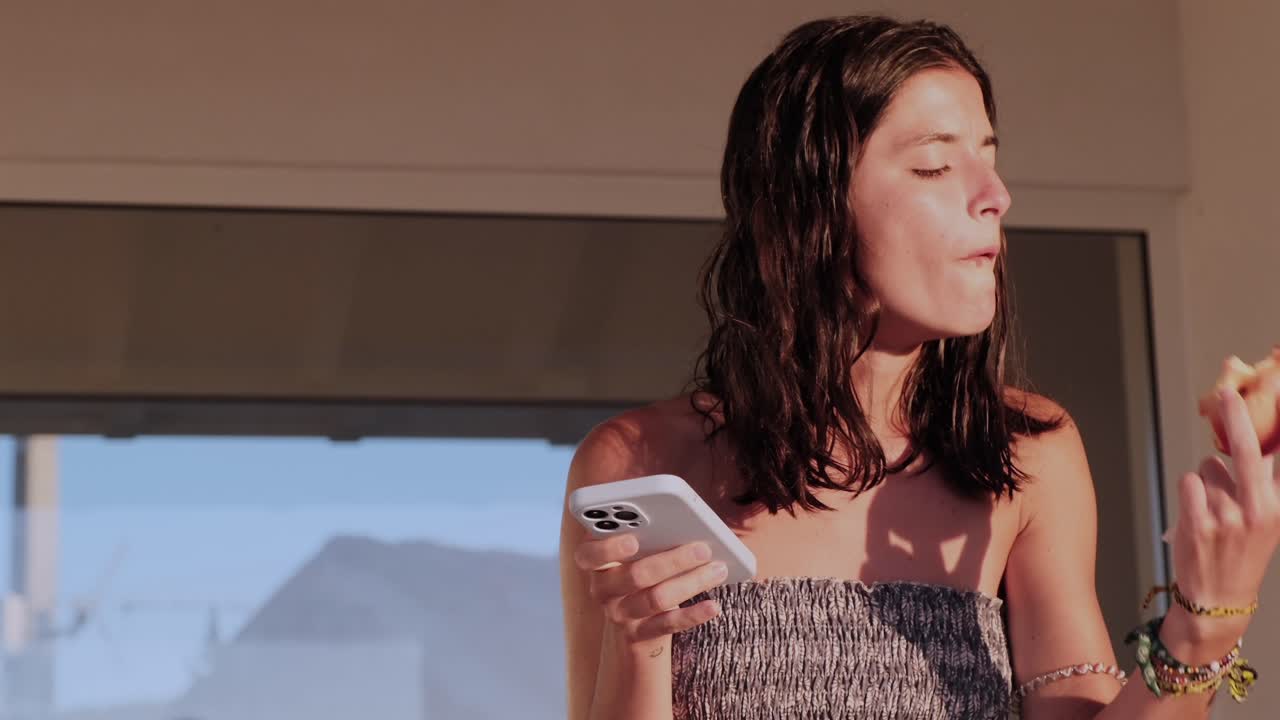 Woman eating fruit while using a smartphone in natural light