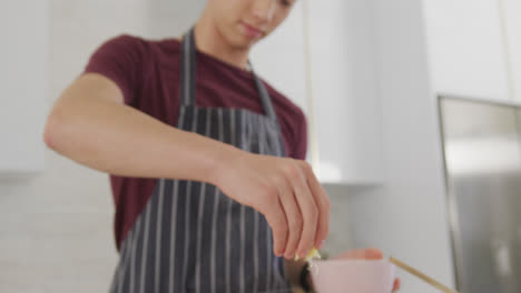 Asian-male-teenager-preparing-food-and-wearing-apron-in-kitchen