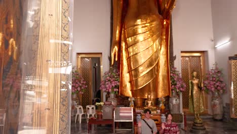 a serene view of the golden buddha statue at wat pho, bangkok, with visitors in a tranquil temple setting