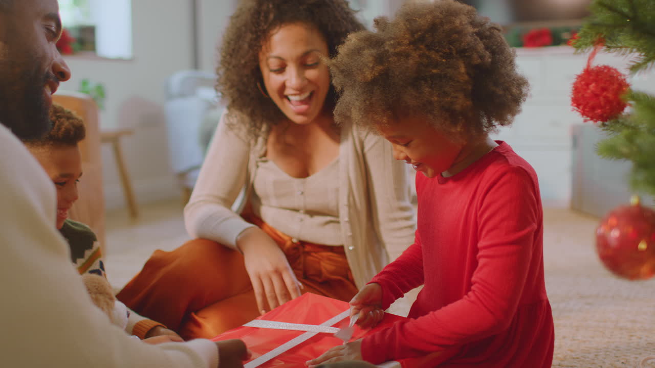 Family Exchanging And Opening Gifts Around Christmas Tree At Home