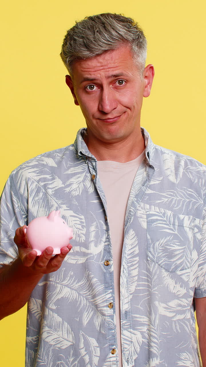 Man holding piggy bank dropping last coin sighing showing saving effort or poor money condition