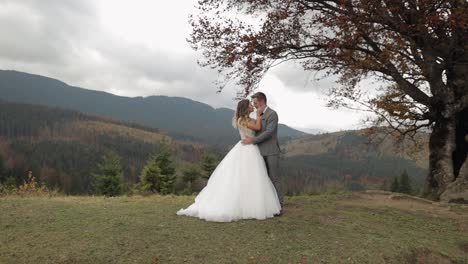 lovely young newlyweds bride and groom embracing, making a kiss on mountain slope, wedding couple