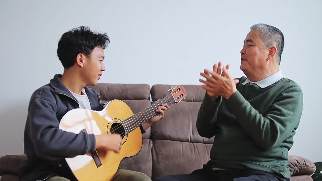 Son plays guitar as father sings along happily on cozy sofa setting