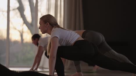 fitness club. female caucasian instructor coaching and adjust correct pose to caucasian girl student at front while others doing follow them.