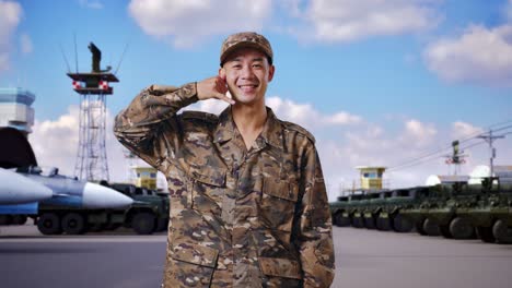 hombre asiático soldado sonriendo y haciendo llamarme gesto a la cámara mientras estaba de pie en el campamento militar