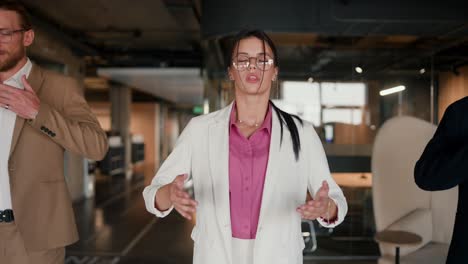 Close-up-shot-of-a-brunette-girl-in-round-glasses-in-a-white-suit-with-a-pink-shirt-doing-breathing-techniques-with-her-colleagues-during-a-break-at-work-in-a-modern-office