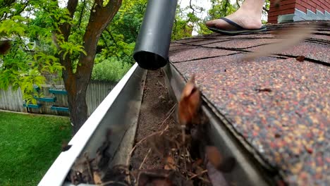 a leaf blower is seen blowing leaves and debris out of a rain gutter on a roof in slow motion