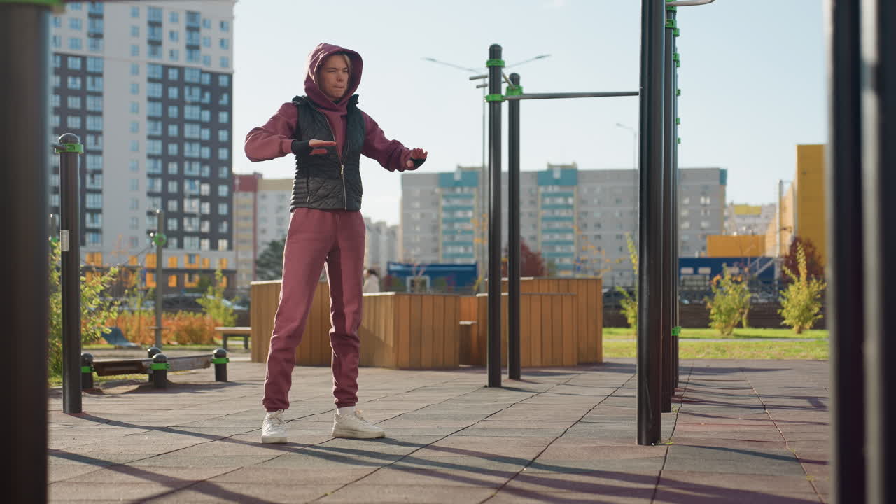 Wellness woman in hoodie and vest stretches arm across chest in outdoor street while people pass under autumn sunlight preparing for exercise with calm focus and serene balance