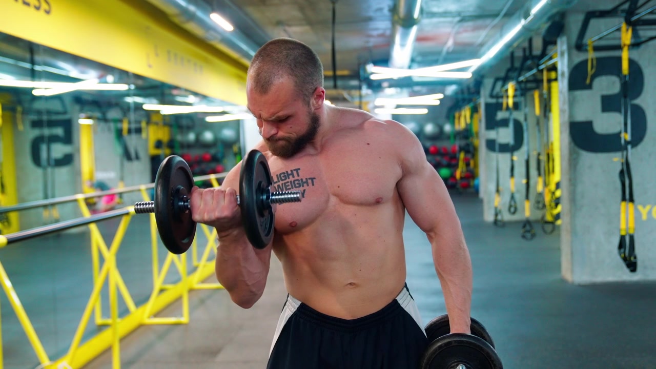 Uomo forte che esegue curl per bicipiti con manubri in palestra
