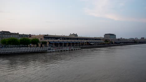 stores and restaurants at quai des marques on the shores of the garonne river in bordeaux france, advancing shot from boat