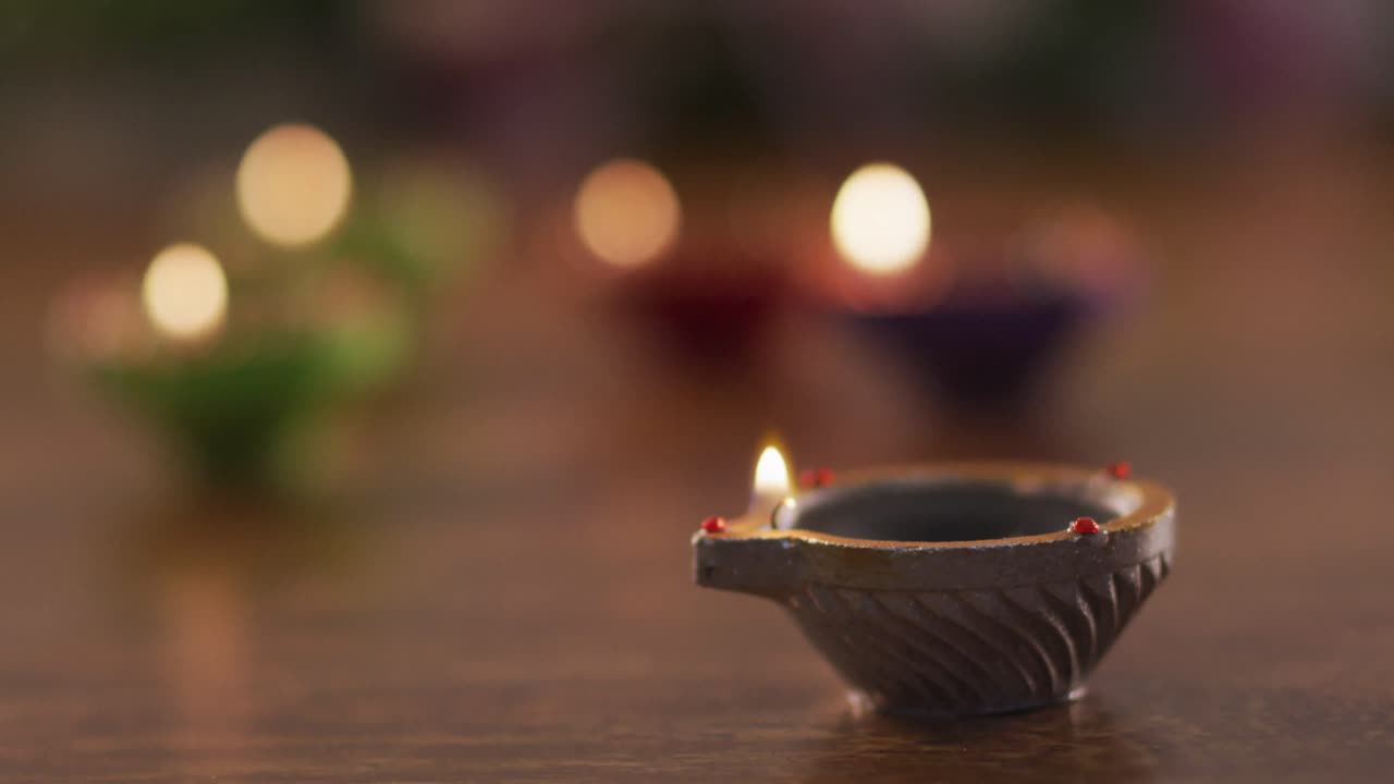 Candele accese in vasetti decorativi di terracotta su un tavolo di legno, fuoco su quello in primo piano, sfondo bokeh
