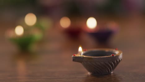 lit candles in decorative clay pots on wooden table top, focus on foreground one, bokeh background