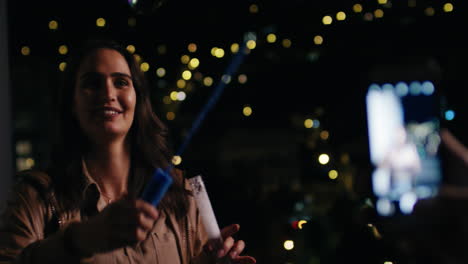 beautiful-young-woman-blowing-bubbles-at-boyfriend-using-smartphone-taking-photos-on-rooftop-at-night-sharing-romantic-evening-with-bokeh-city-lights-in-background