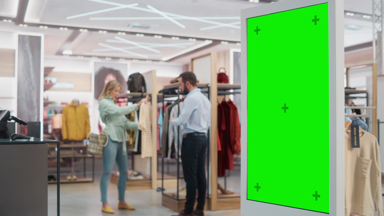 Customer Using Floor-Standing LCD Touch Display with Green Screen Chroma Key Mock Up while Shopping in Clothing Store. She is Checking for Information, Looking at a Floor Plan, Choosing Items Online.