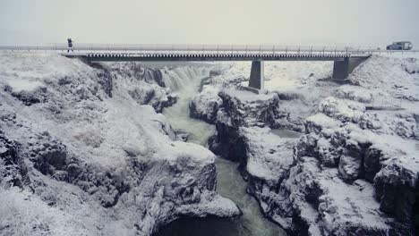 hombre caminando a través de un puente en el cañón de kolugljufur islandia en invierno - tiro ancho