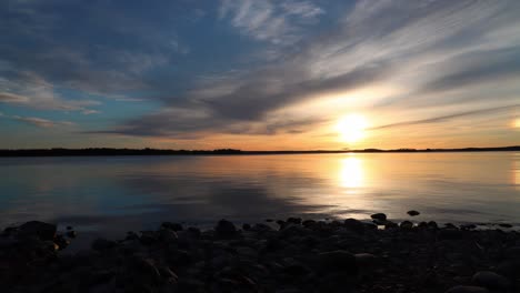 sunrise time lapse with clouds passing in front of an orange sun over a large lake