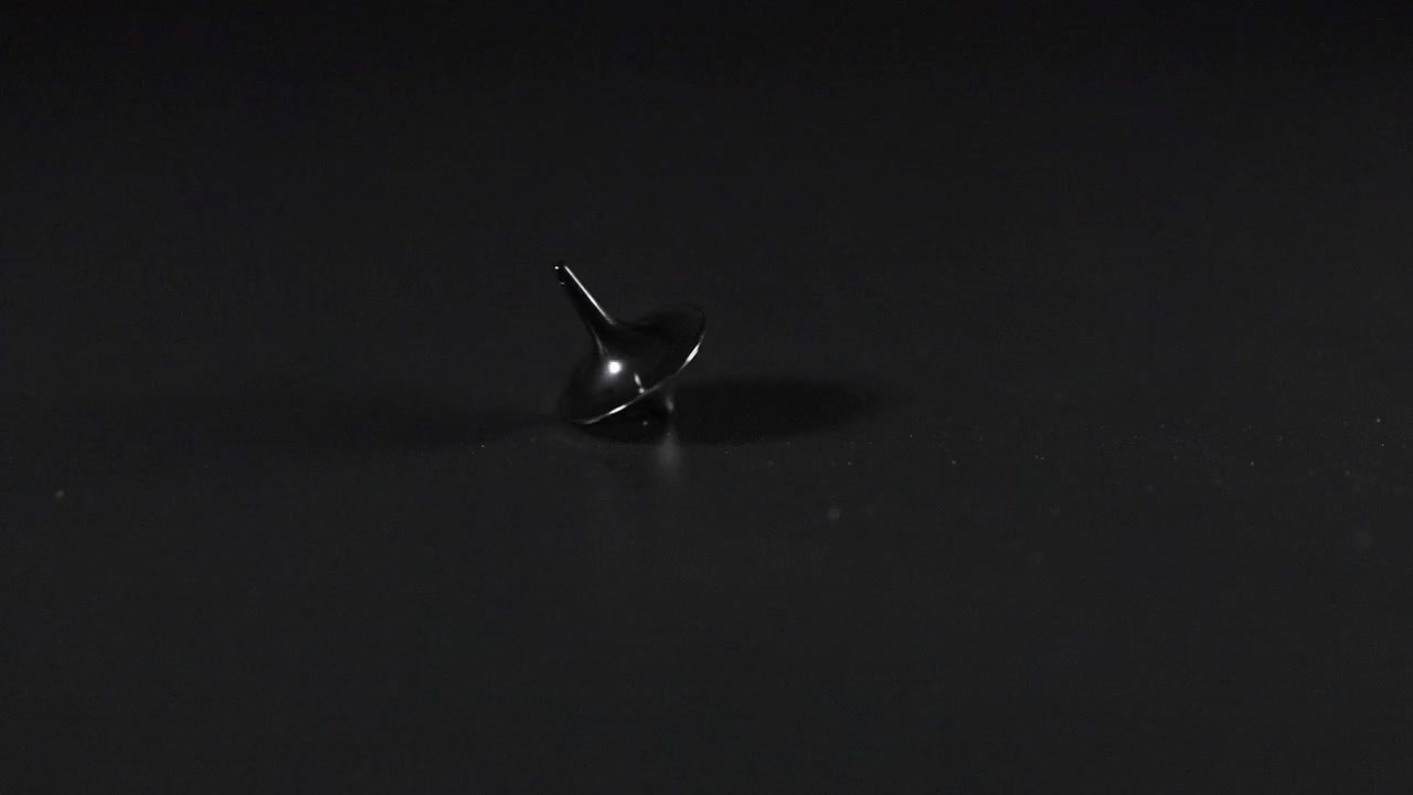 A spinning top rotating on a dark surface
