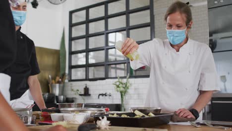 Caucasian-female-chef-teaching-diverse-group-wearing-face-masks