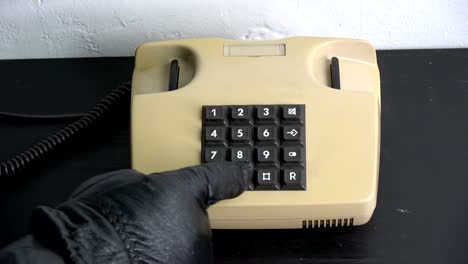 robber gangster hand with black leather glove pressing numbers buttons on classic  telephone