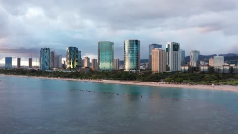 aerial wide rising shot of the sun reflecting off buildings in downtown honolulu, hawaii at sunset