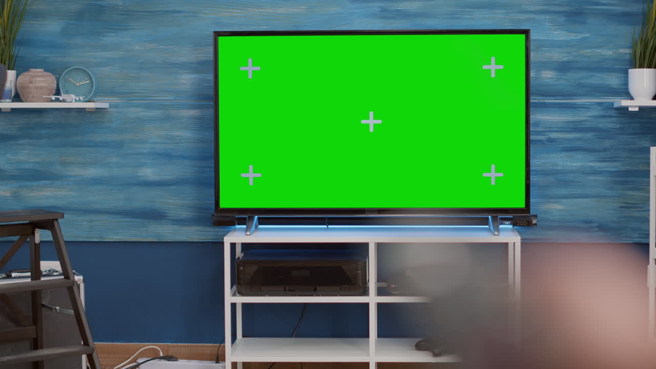 Selective focus of hand holding remote control and switching channels on green screen tv