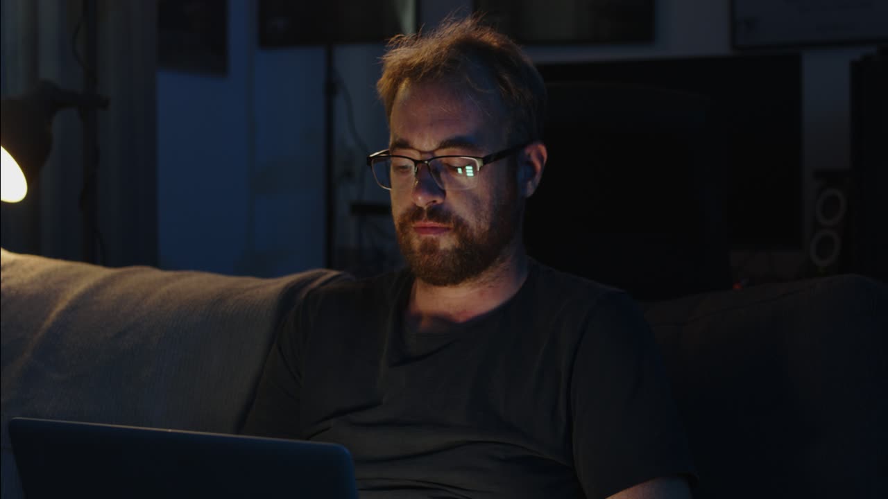 A man is sitting in his living room couch and working on his laptop late at night