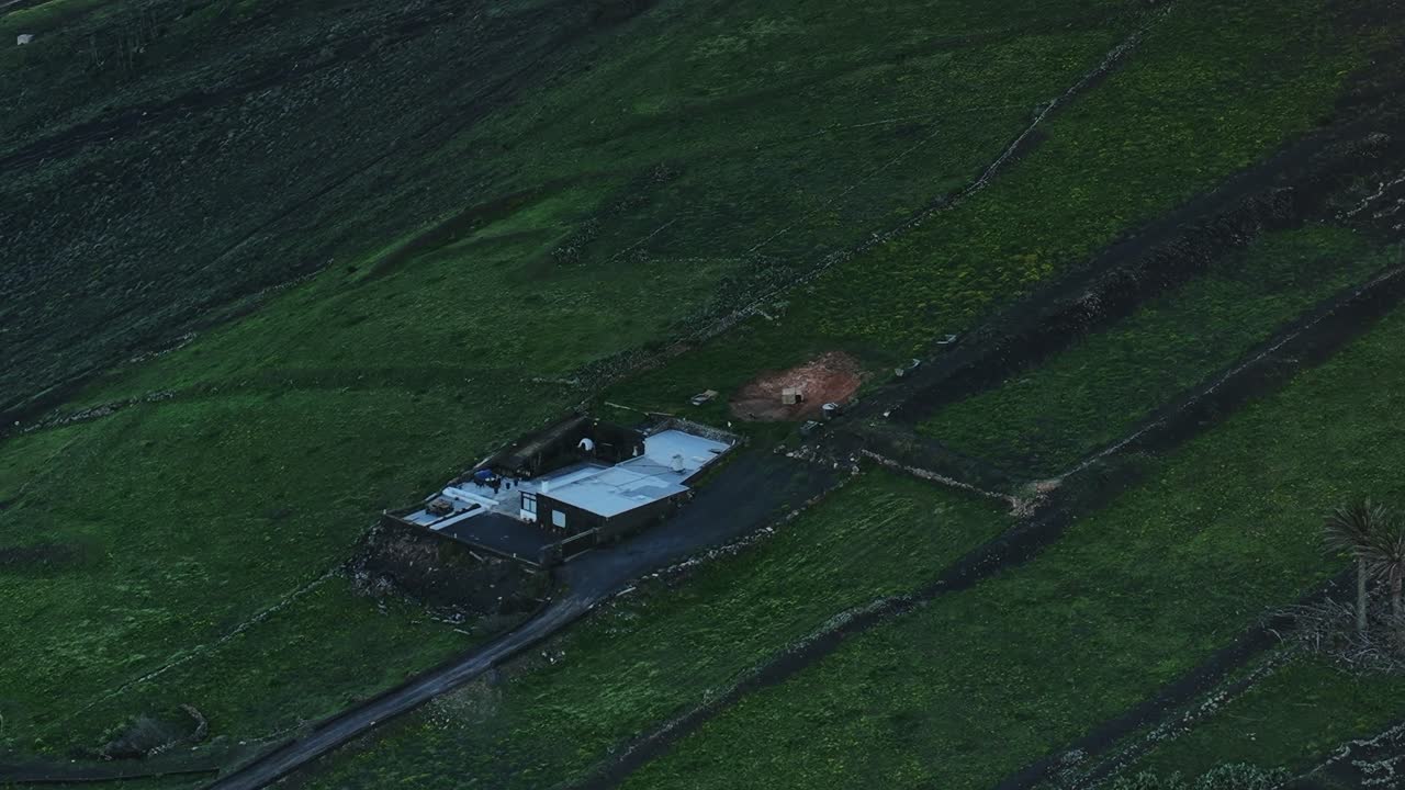 Utsikt över ett hus på Lanzarote, Spanien, omgivet av gröna fält och kullar.