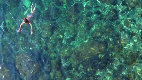 two tourists swimming in the transparent waters of ibiza, spain. dramatic aerial view flight drone camera pointing down