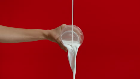 mujer irreconocible vertiendo leche en un vaso en el estudio sobre fondo rojo.