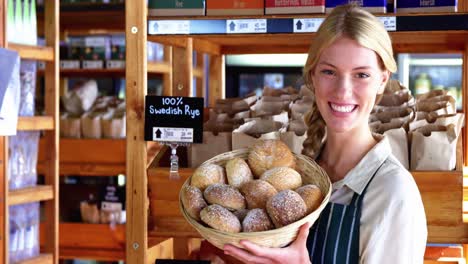 smiling female staff holding basket of sesame breads at bread counter