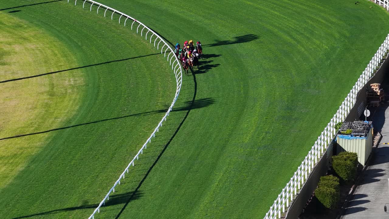 Several jockeys ride racehorses around a curved turf track in bright daylight, captured from above with smooth drone movement at an Australian racecourse