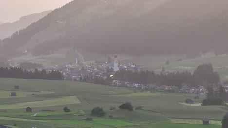 idyllic village nestled in rolling green fields at sunrise with misty mountains in the background