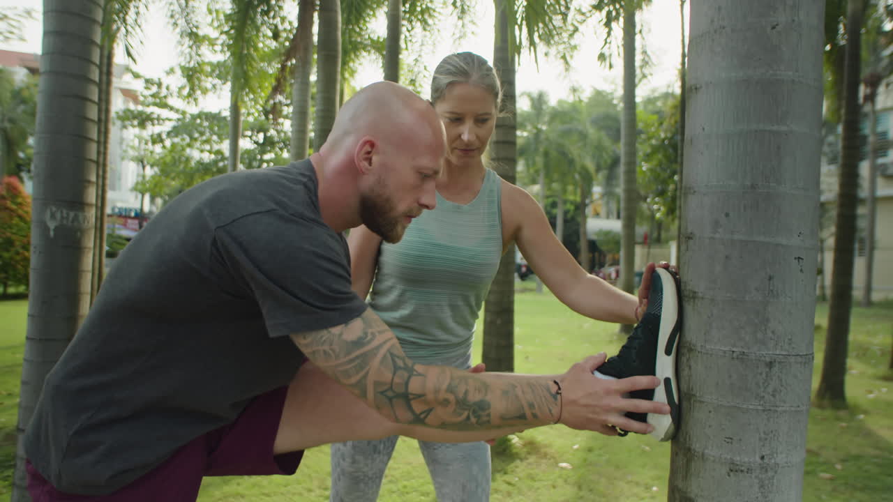 Man Stretching in Park with Female Personal Trainer