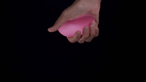 a hand holding a pink heart and then crushing it, dark background and copy space