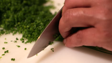 chef slicing green onion chives using a sharp knife on a white chopping board