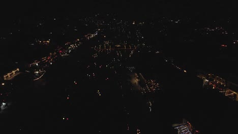 Night-aerial:-Lit-up-boats-navigate-dark-city-river-in-Hoi-An,-Vietnam