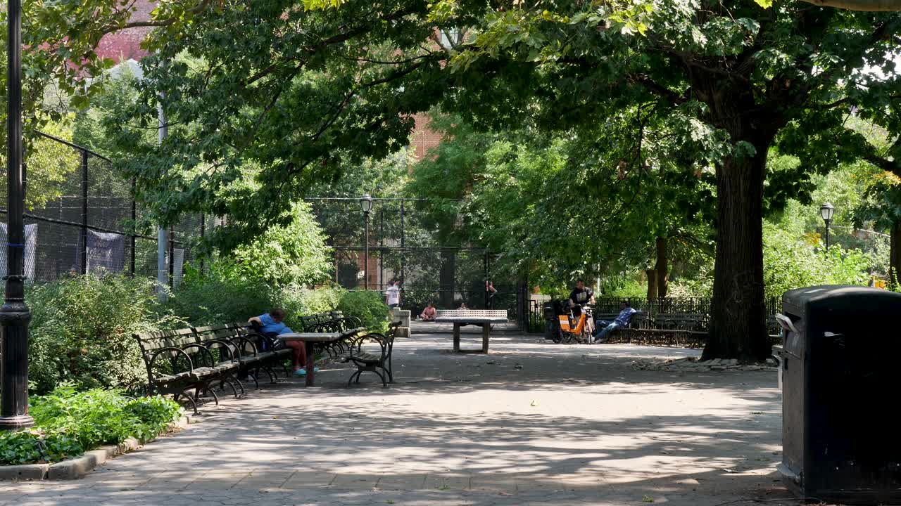 Slow motion landscape of person sitting on public park bench seat in suburban outdoors neighbourhood Tompkins Park Square New York City USA America