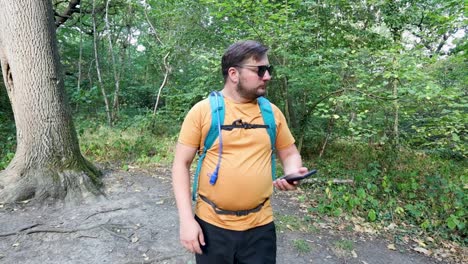 Junger-Mann-Mit-Rucksack-Und-Sonnenbrille-Kommt-Aus-Dem-Wald,-Schaut-Sich-Um-Und-überprüft-Den-Kompass