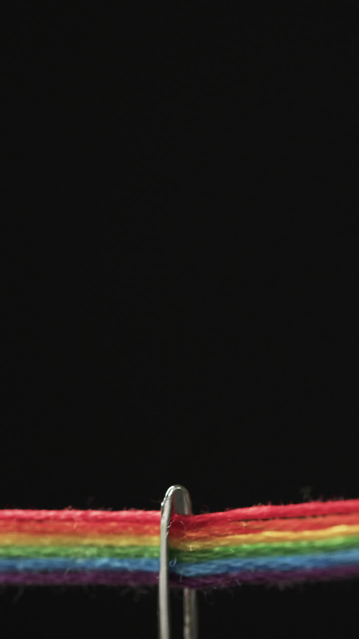 Vertical video of micro of needle with rainbow coloured threads and copy space on black background