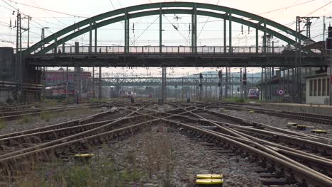 Cruzando-Las-Vías-Del-Tren-En-La-Estación-De-Tren-Con-Los-Coches-Circulando-Por-El-Puente-En-Segundo-Plano.