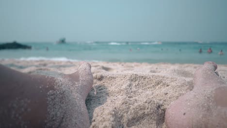 fellow-strong-feet-lie-on-yellow-beach-lit-by-sun-closeup