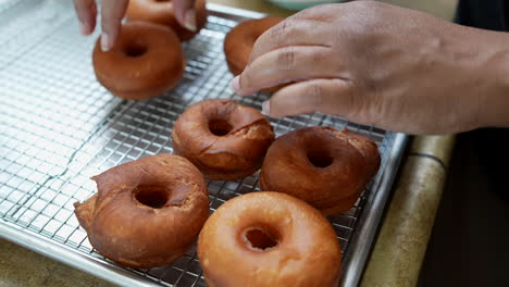 Slowmo-Closeup-on-Hands,-Woman-rearranges-fresh-donuts-on-wire-cooling-rack