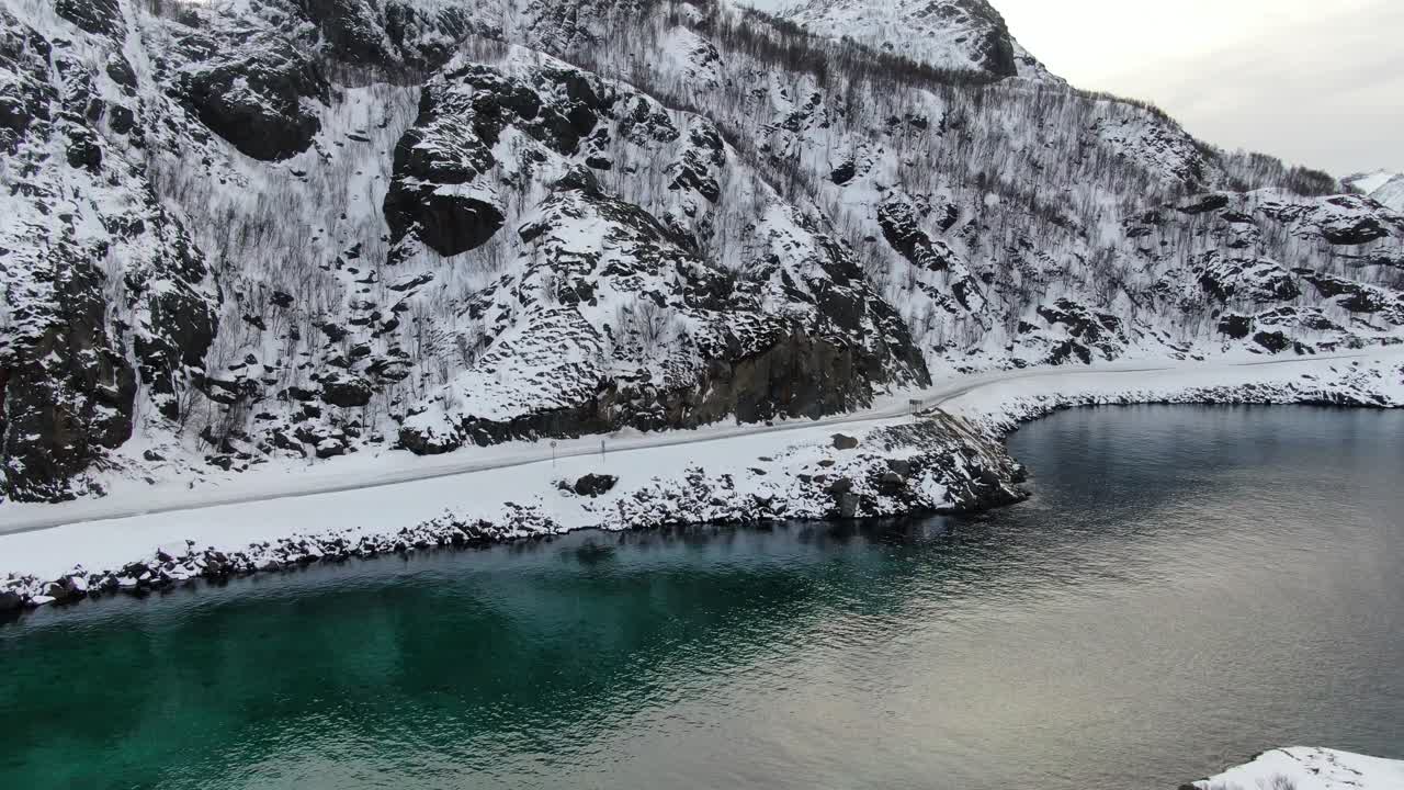 vista de avión no tripulado en el área de tromsø en invierno levantándose desde el suelo que muestra un mar cristalino turquesa que rodea una isla en noruega