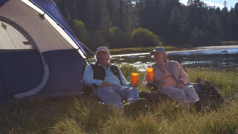 senior couple sitting outside tent near lake, closer-in shot