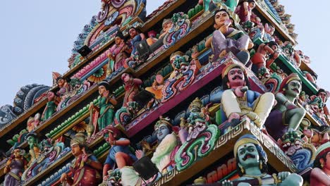 camera tilts upward along a vibrant, intricately decorated hindu temple gopuram under daylight, highlighting colorful statues and detailed architectural carvings