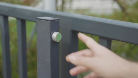 close up of finger pressing green release button, opening modern metal gate